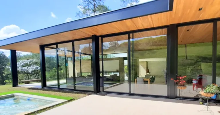 Casa con puertas y ventanales de vidrio y aluminio frente a una piscina