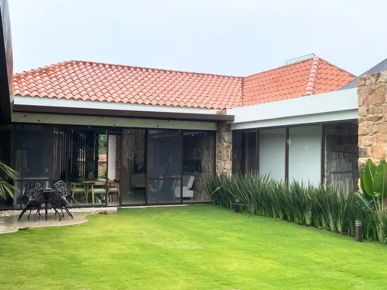 Casa campestre con techo de teja y ventanería en vidrio y aluminio hacia el jardín