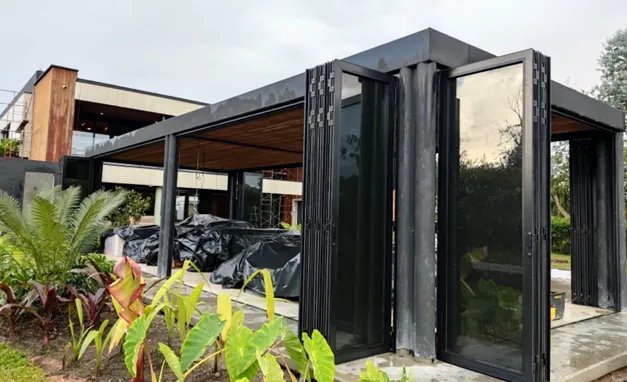 Cerramiento en vidrio y aluminio negro con puertas plegables abiertas