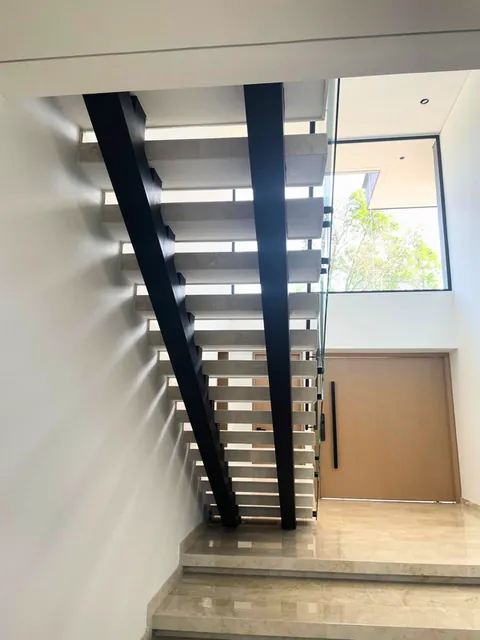Escalera con vigas metálicas negras y huellas claras junto a ventanal